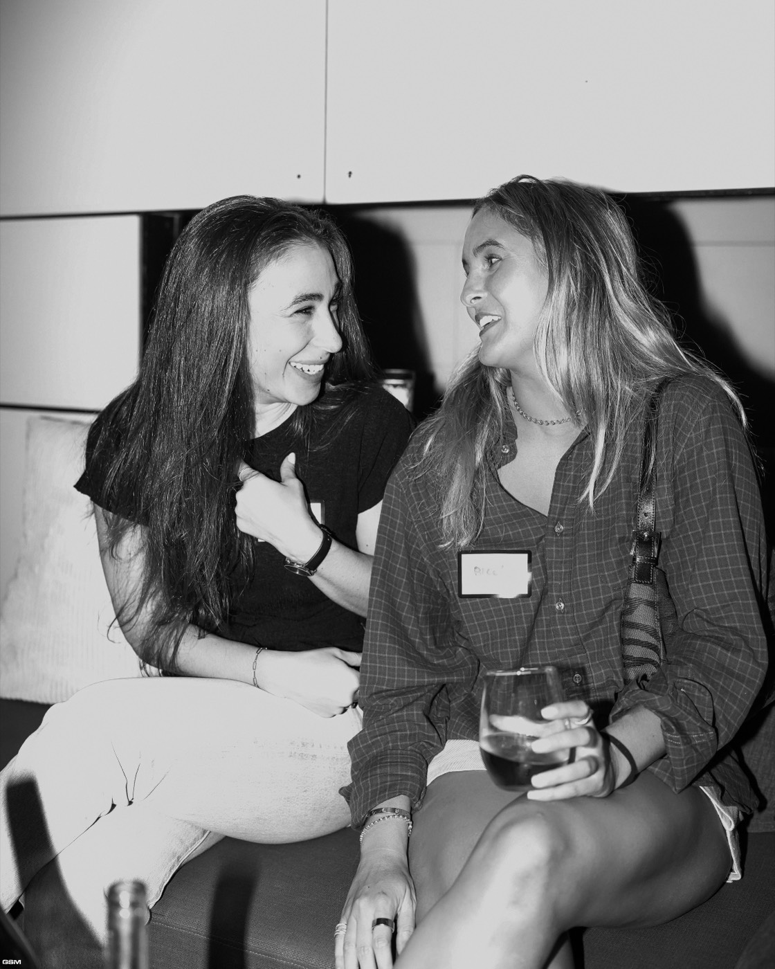 Two friends laughing on a couch, in black and white